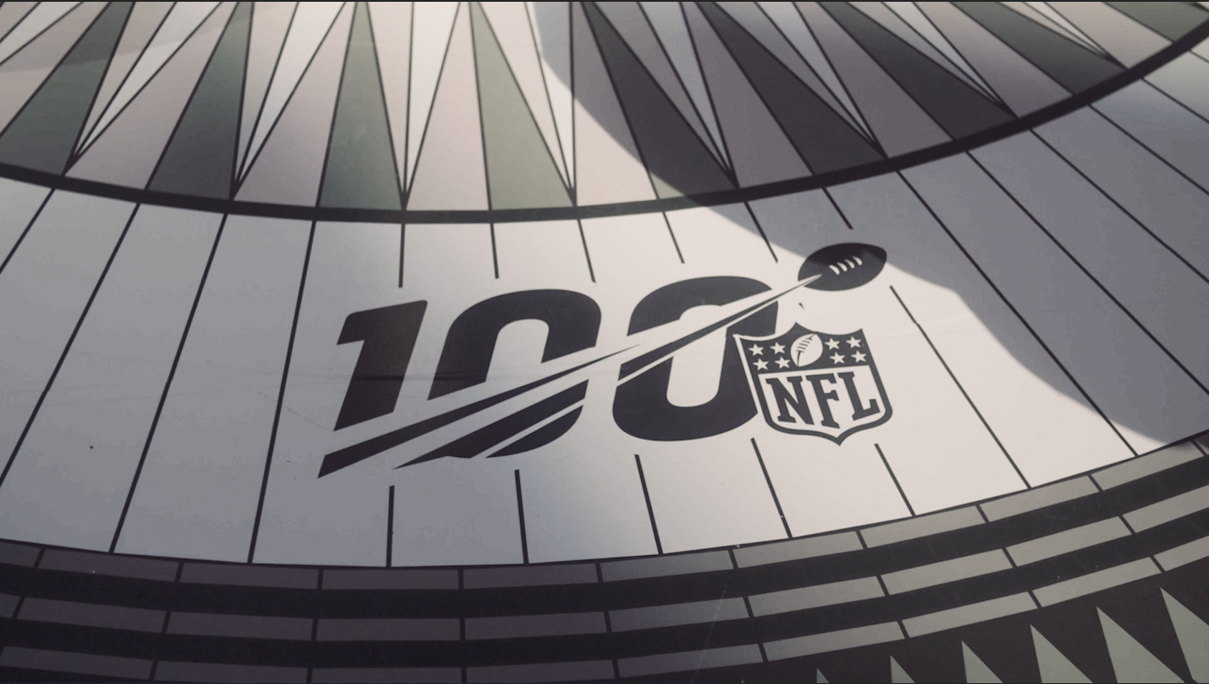 NFL logo in front of the number one-hundred with a football soaring through the number 